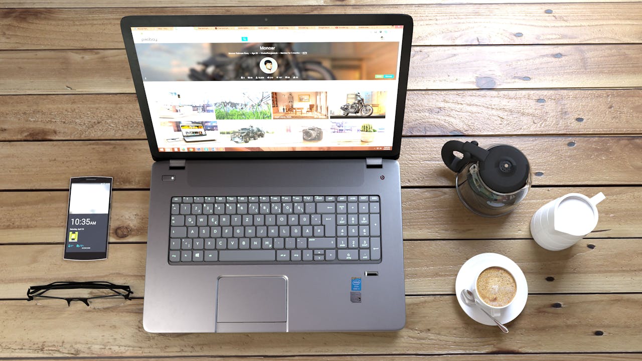 Silver Laptop Next to Coffe Cup Smartphone and Glasses